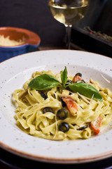 Closeup view of Pasta with chicken, olives and cheese on ceramic white plate with glass of white wine on table