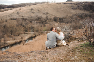 Naklejka na ściany i meble Love, romance and people concept - happy young couple hugging sitting on the edge of a cliff outdoors