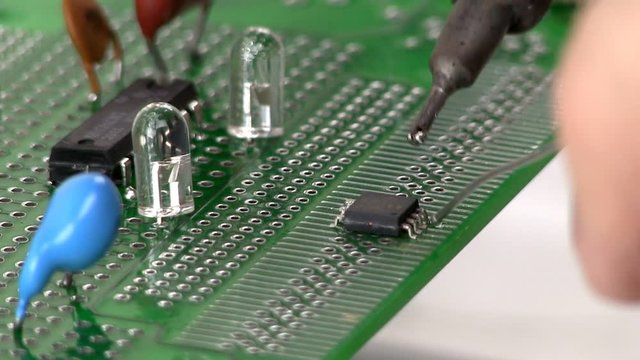 An electrical engineer builds a circuit design by soldering a surface mount IC to a breadboard by hand
