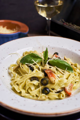 Closeup view of Pasta with chicken, olives and cheese on ceramic white plate with glass of white wine on table