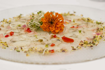 Carpaccio of white fish with pistachio nuts crumble and sprouts of green peas.