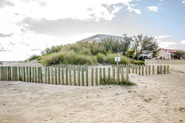 Sand dune with wooden sand fence and houses at background at south France