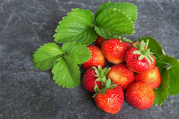 Strawberries and green leaves on a black stone
