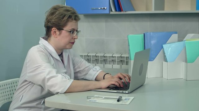 Concentrated female doctor in glasses typing on laptop in her office