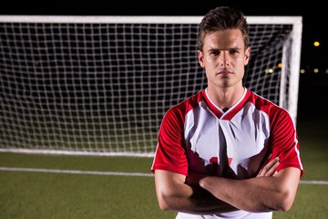 Confident male soccer player standing with arms crossed against goal post on field