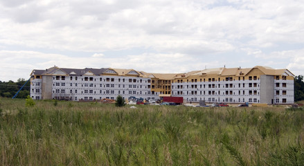 Housing construction with foreground field and clouds sky.