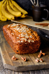 Banana bread loaf with oats and walnuts on wooden cutting board. Closeup view