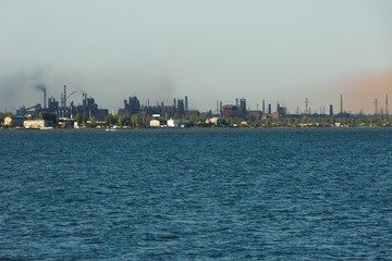 Big steel factory metallurgical plant with sea harbor and lots of pipes throwing dark dirty smoke and dust in the atmosphere. Ecological air and water pollution concept