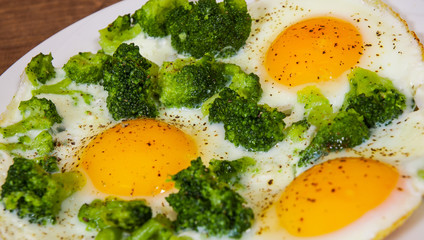 Fried eggs with broccoli in plate on the brown wooden table background