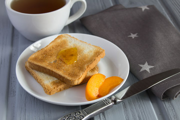 Bread toast with apricot jam and tea on the grey wooden background
