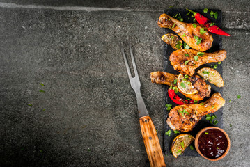 Summer food. Ideas for barbecue, grill party. Chicken legs, wings grilled, fried on fire. With hot chili pepper, lemon and bbq sauce. Dark stone table, Copy space top view