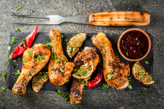 Summer food. Ideas for barbecue, grill party. Chicken legs, wings grilled, fried on fire. With hot chili pepper, lemon and bbq sauce. Dark stone table, Copy space top view