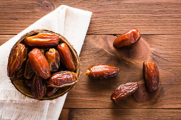 Sweet dried dates fruit in a small bowl on napkin on wooden table. Top view