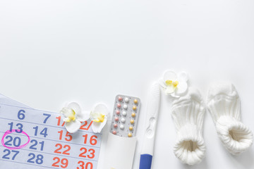 Pregnancy planning. Pregnancy test, calendar and booties on white background top view copyspace