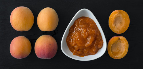 Apricot jam and apricots arranged on black wooden background