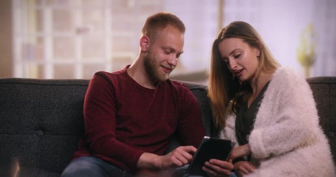 Young cattractive ouple sitting on sofa using tablet