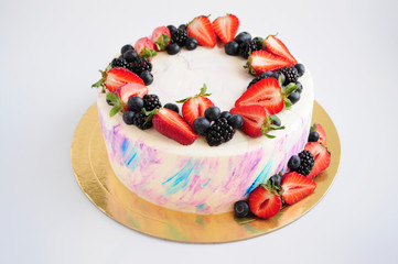 Cake with whipped blue and pink cream, fresh strawberries, blueberries and blackberry. Picture for a menu or a confectionery catalog.