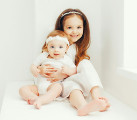 Two cute sisters children together at home in white room near window