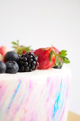 Cake with whipped blue and pink cream, fresh strawberries, blueberries and blackberry. Close-up. Picture for a menu or a confectionery catalog.