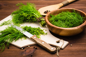 Chopped fresh dill on a cutting board and dill in a wooden bowl on the table