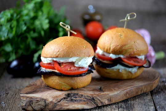 Vegan burgers with corn bun with soft cheese, eggplant and tomatoes on a wooden background.