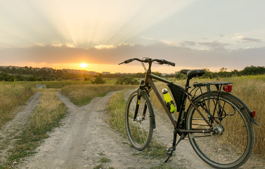 Obraz premium The bicycle stands on a village road that is divided into two parts. Sunset time.