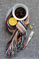 Treatment methods: thermometer, jam, lemon and warm scarf for cold or throat pain on the grey knitting background
