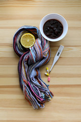 Treatment for cold and throat pain. Thermometer, jam, lemon and tablets on the light wooden background