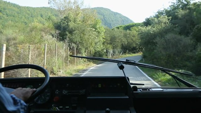 Coach going down narrow road aligned with plants, view from behind windshield