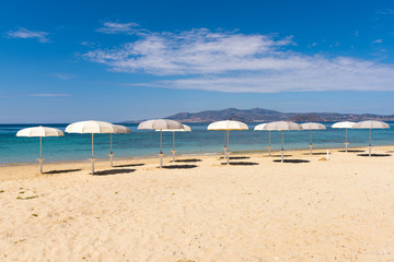 White parasols on Idyllic tropical beach with sand, turquoise sea water and blue sky. Naxos island. Cyclades, Greece.	