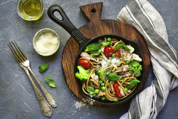 Whole wheat pasta with chicken fillet and vegetables in a cast iron  pan.Top view.
