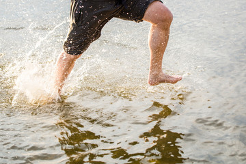 A man running along a beach and splashing water