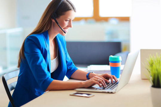 Portrait of beautiful business woman working at her desk with headset and laptop.