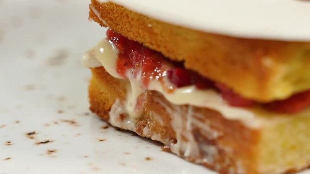 Sponge cake with strawberries, jam and whipped cream with a cut out piece, closeup