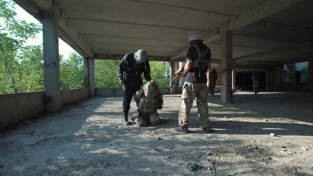 Two men in uniform attacking terrorists and freeing hostage inside of ruined building.