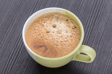 Hot black coffee with foaming in green cup placed on dark wooden table, morning coffee concept.