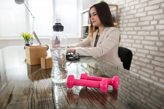 Water Bottle And Pink Dumbbells On Office Desk