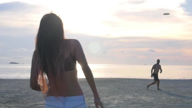 Young Sport Couple Playing Frisbee on Beach At Sunset. Slow Motion. HD, 1920x1080. 