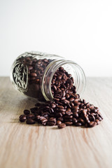 Fototapeta na wymiar Spilled coffee beans from mason jar on wood grain texture