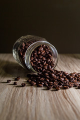 Spilled coffee beans from mason jar on wood grain texture