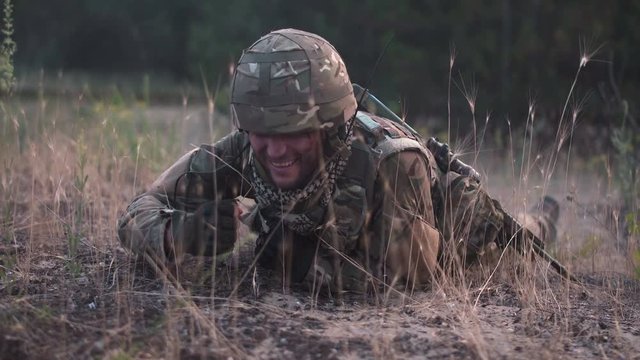 Man in military uniform with gun crawling alone on ground in field.