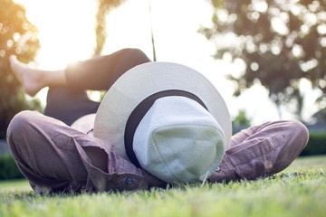 Asian trendy hipster man wearing  a white cap, pink shirt and black jean while lying on the green...