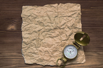 Compass and blank crumpled brown page paper on wooden table. Adventurer, treasure hunt or travel concept.
