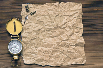 Compass and blank crumpled brown page paper on wooden table. Adventurer, treasure hunt or travel concept.