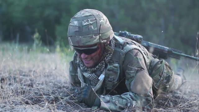 Slow motion man in military uniform with gun crawling alone on ground in field.