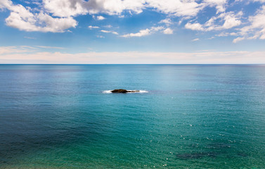 Single rocky island on calm azure blue sea.
