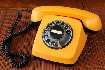 Close up of an old, scratched orange rotary dial telephone on a bamboo mat