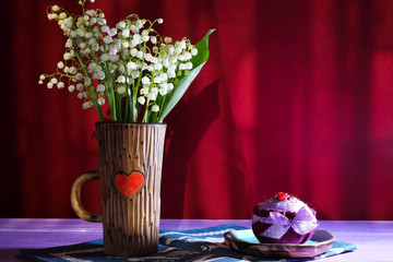 Bouquet of lily-of-the-valley flowers in a ceramic cup with a heart on a blue napkin and textile...