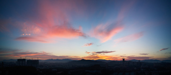 Beautiful panorama natural sunset sunrise over silhouettes city skyline and amazing orange cloud blue sky above it .