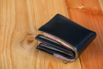 Black men leather wallet with banknotes on wooden table in vintage tone.